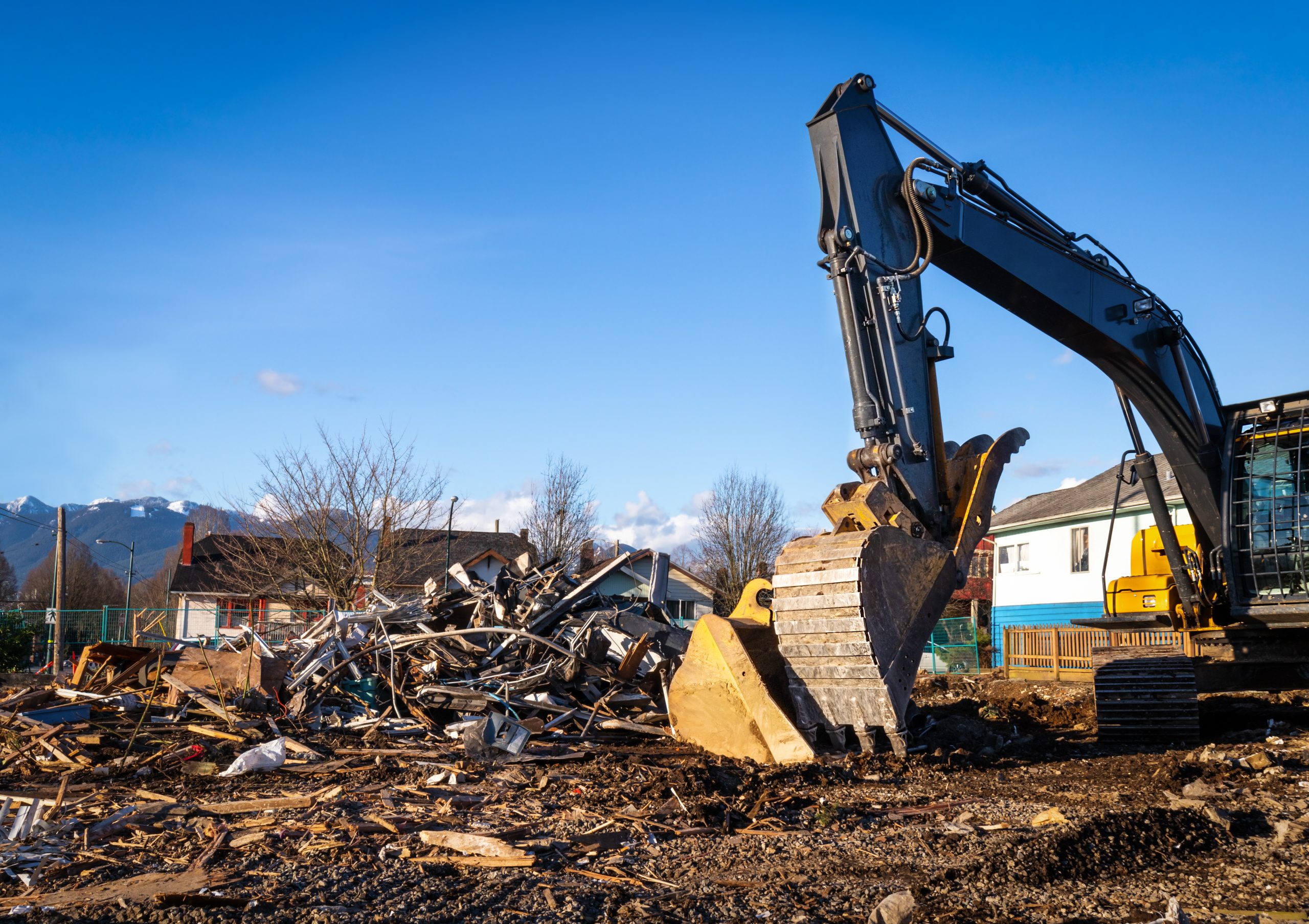 Demolition bulldozer in front of building rubble. Bucket is down, side view. Yellow construction machine with residential buildings and mountains in background.